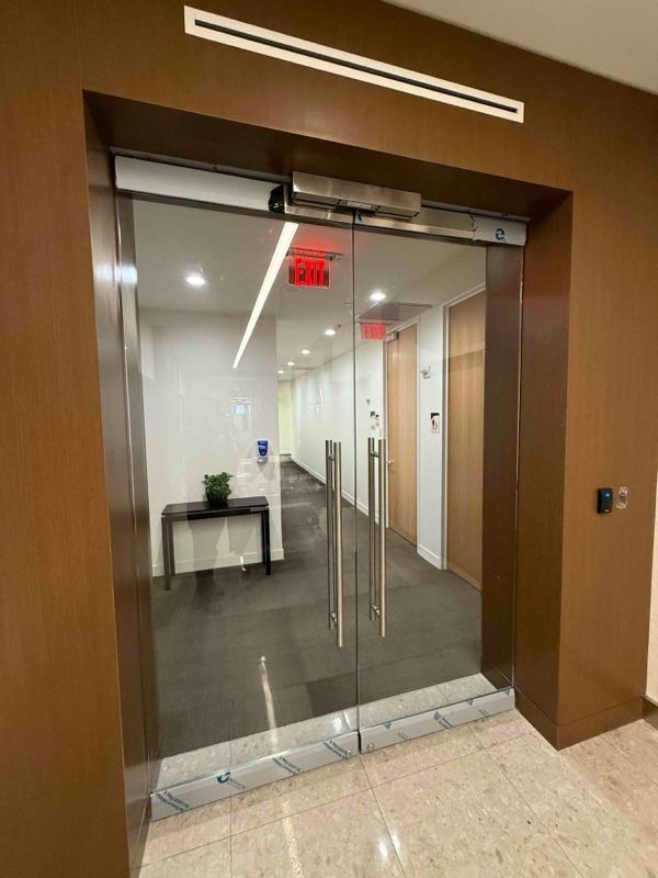 Double magnetic lock entry on a frameless glass Herculite door at an office lobby entrance